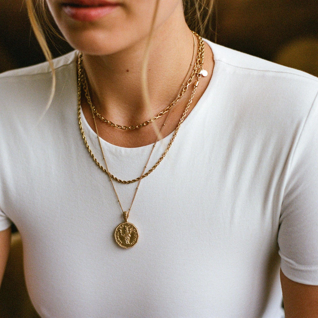 Close-up of woman's neck wearing layered gold chains with a medallion pendant on white shirt