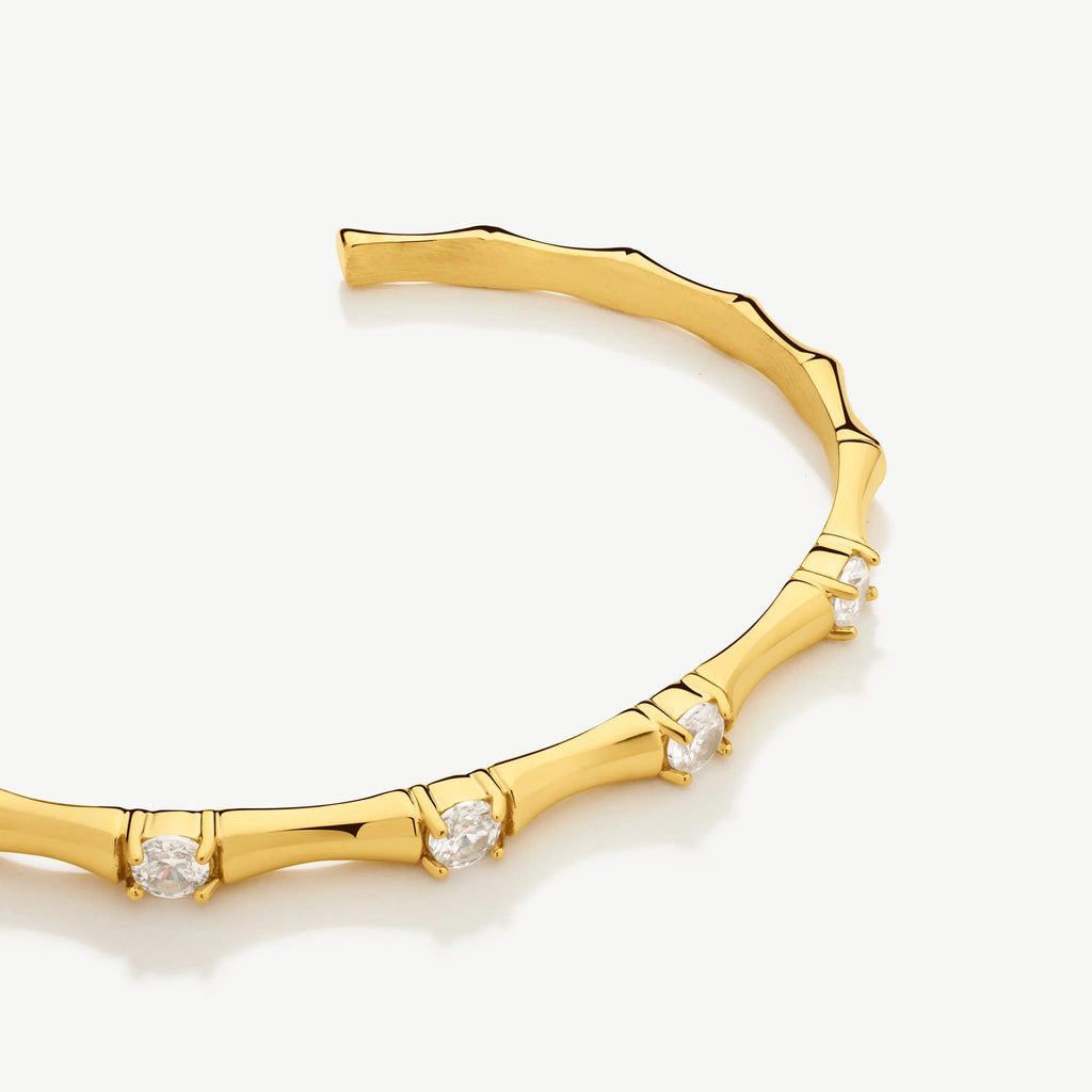 Gold bamboo-style bracelet with embedded clear gemstones on white background