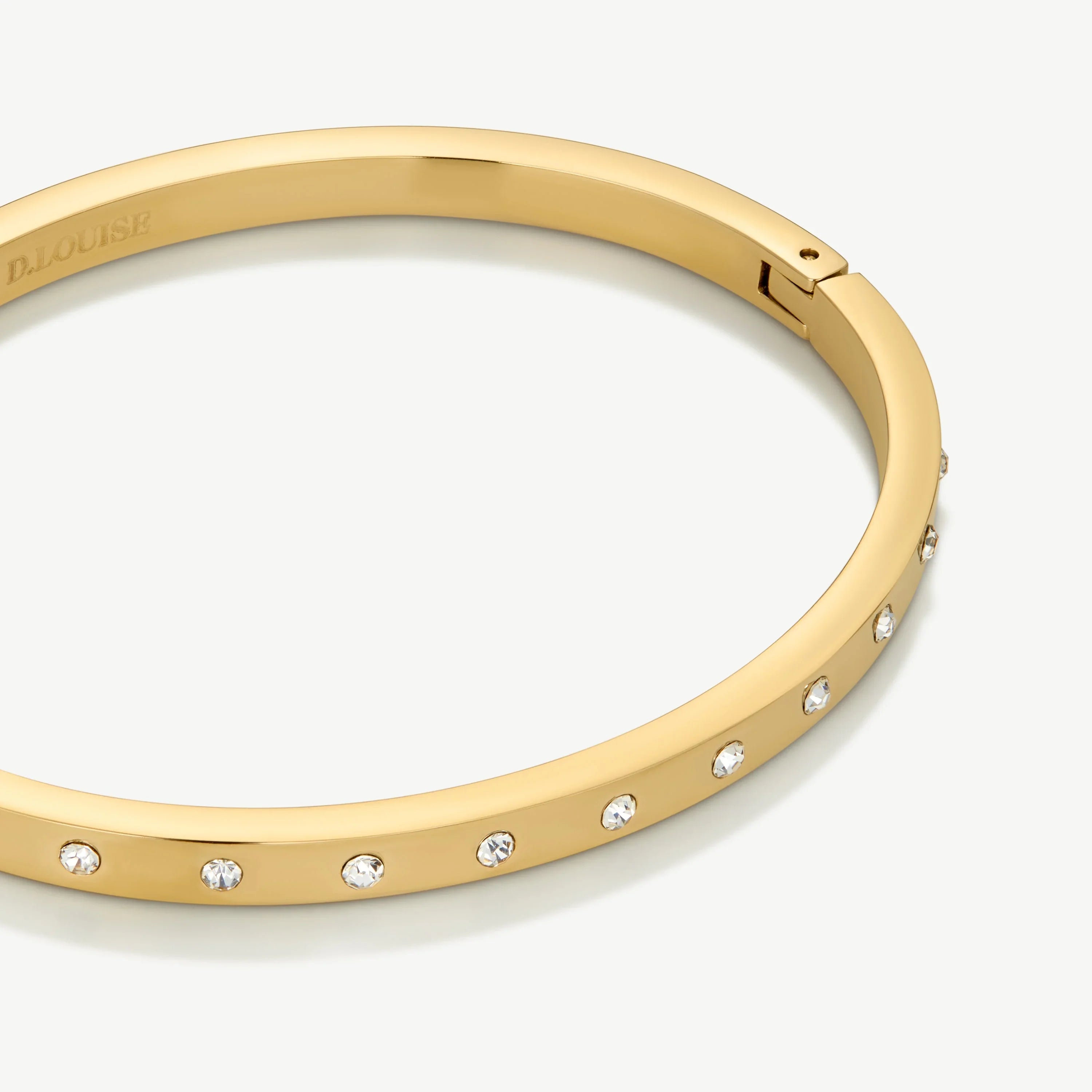 Gold bangle bracelet with embedded clear crystals on a white background