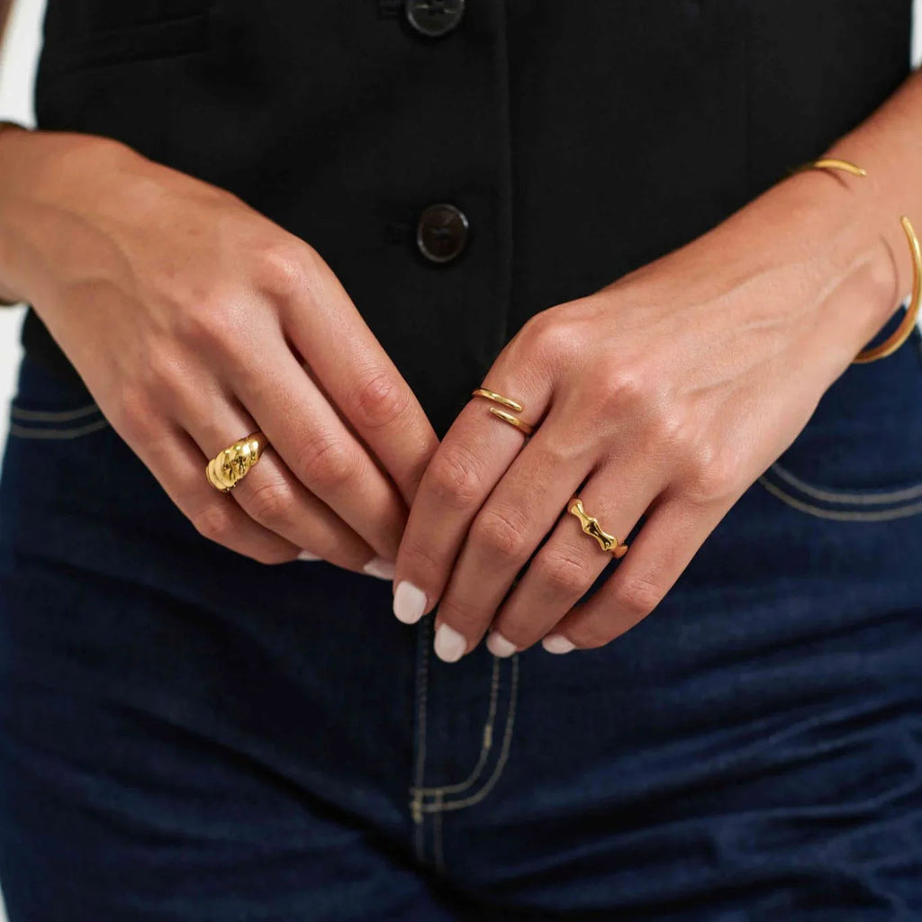 Close-up of hands wearing three gold rings and a gold bracelet, with white nail polish, black top, and blue jeans