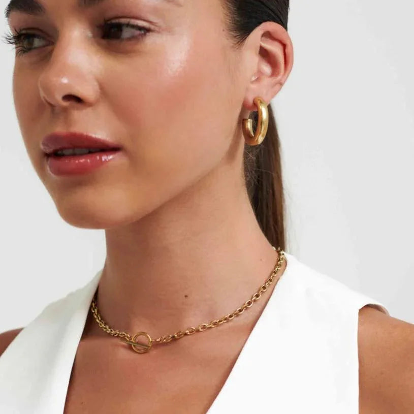 Close-up of woman wearing gold hoop earrings and gold chain necklace with toggle clasp