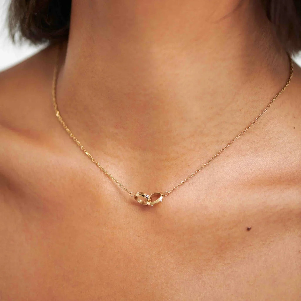 Close-up of woman wearing delicate gold chain necklace with two interlocking rings pendant