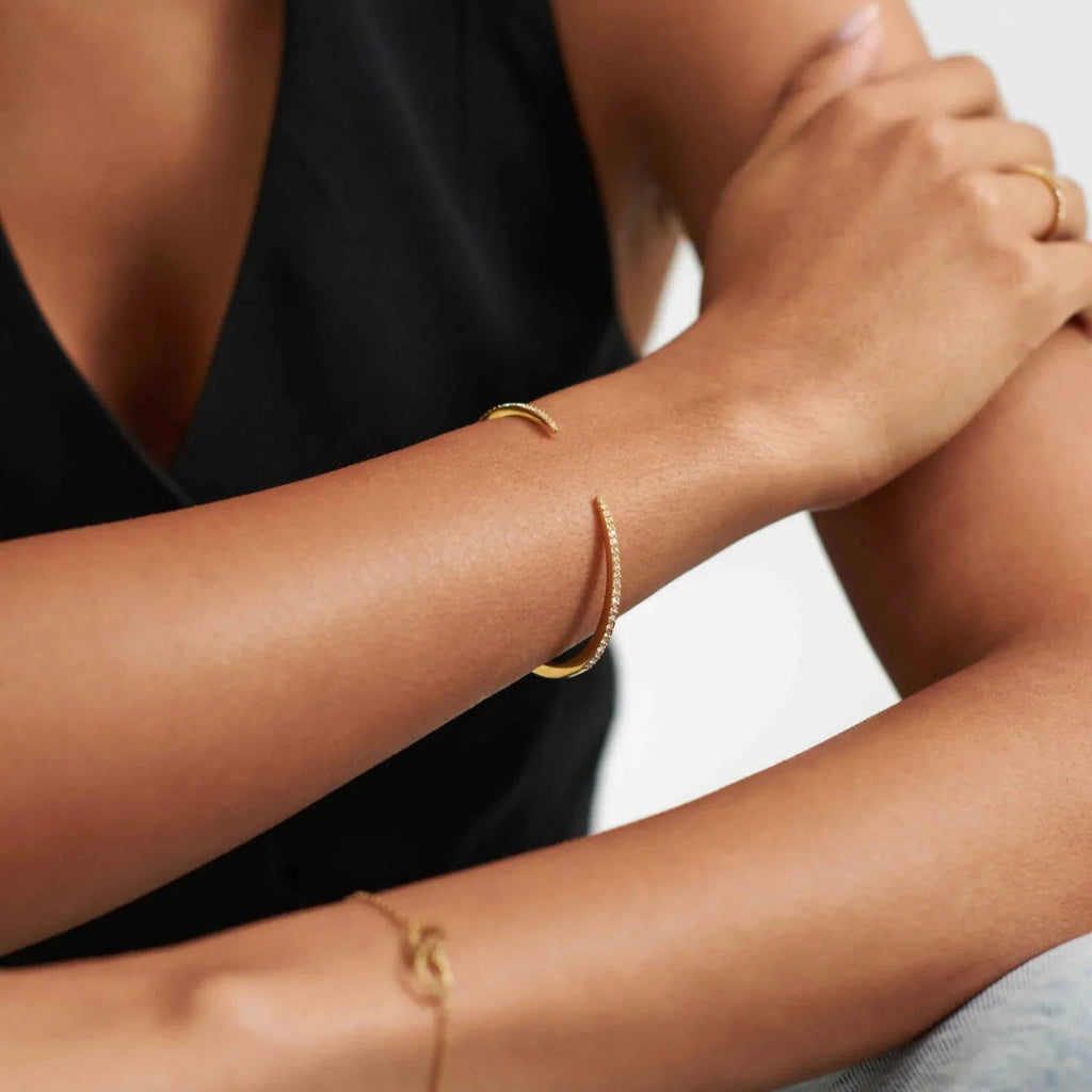 Close-up of woman's arm wearing gold open cuff bracelet with small crystals on black sleeveless top