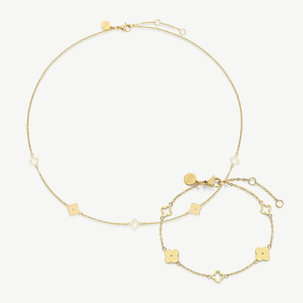 Gold necklace and bracelet set with clover-shaped charms on a white background