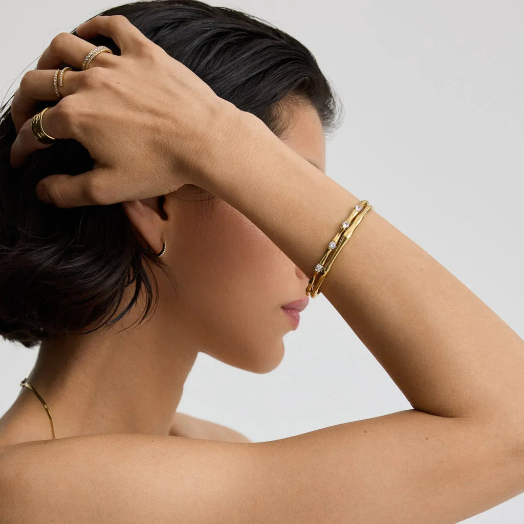 Close-up of woman wearing gold bamboo-style bracelets with diamonds and gold rings on fingers