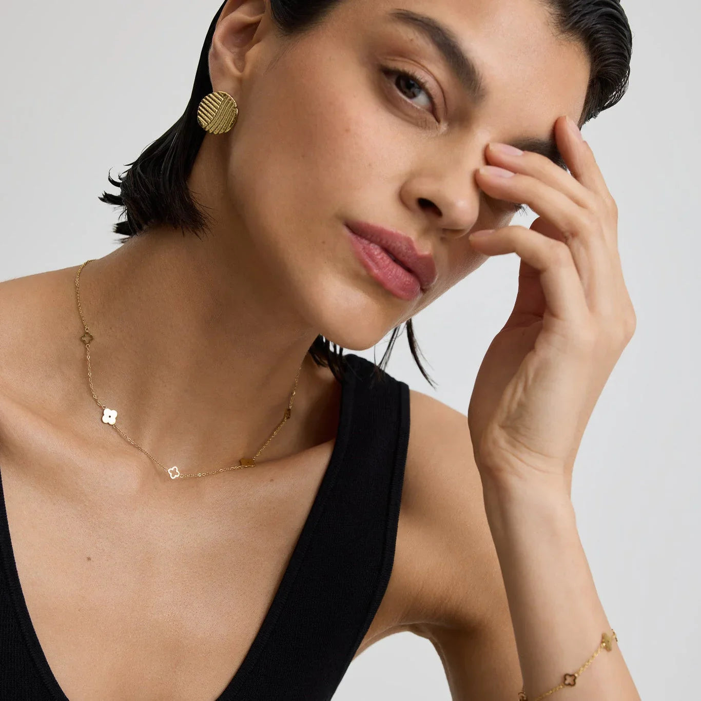 Woman wearing gold textured round coin earrings, gold flower necklace, and bracelet with black tank top