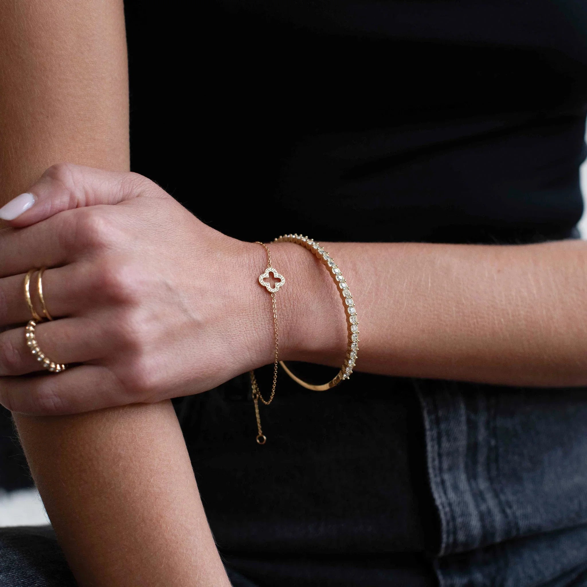 Close-up of woman's arm with gold bracelets and rings, wearing a black top and dark jeans