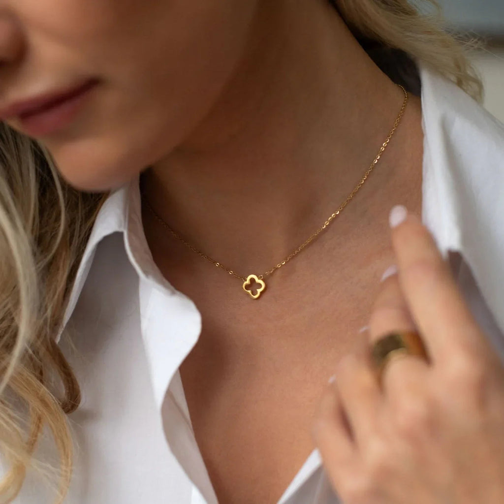 Close-up of a woman wearing a delicate gold clover pendant necklace with a white shirt