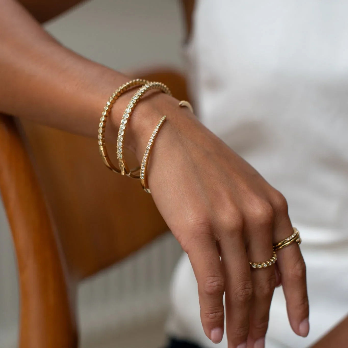 Hand wearing gold bracelets and rings with clear gemstones on light skin