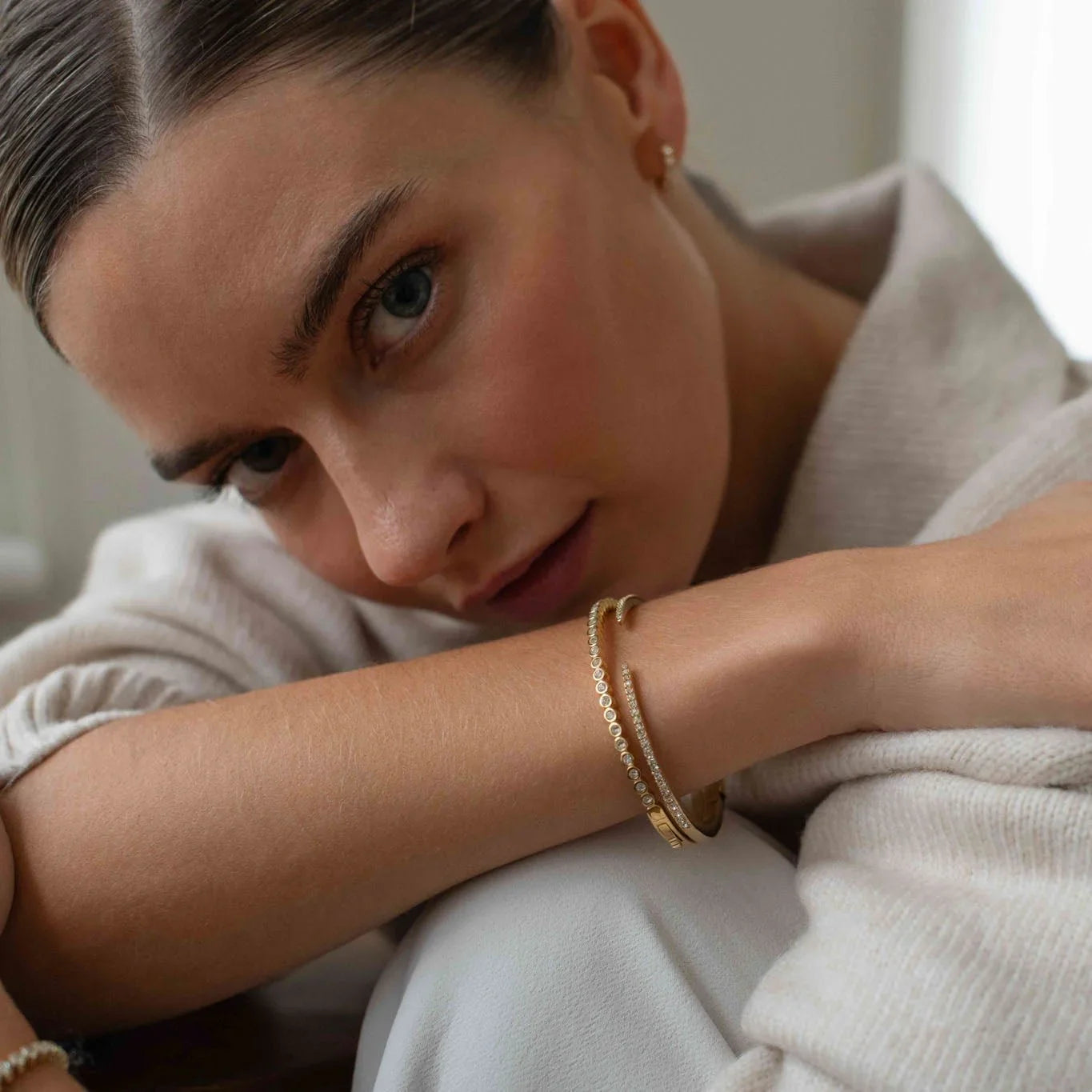 Close-up of woman wearing elegant gold and diamond bracelets with cream knitwear background