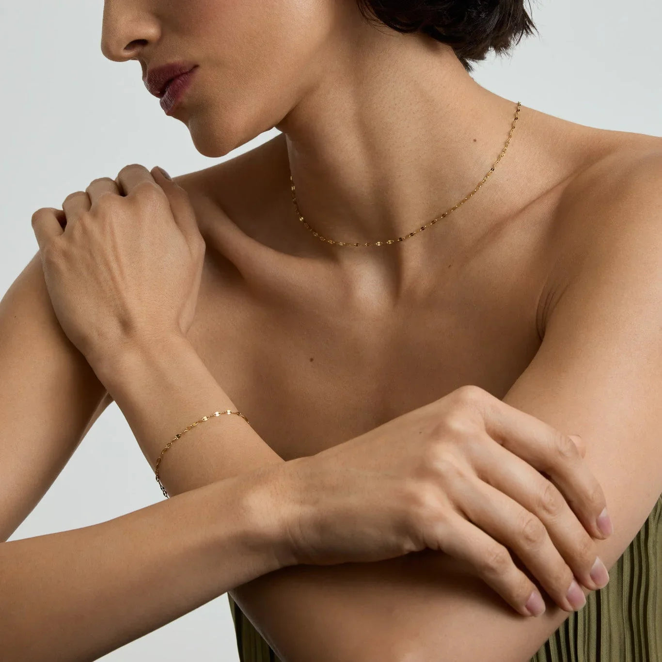 Close-up of a woman wearing a delicate gold chain necklace and matching bracelet against a neutral background