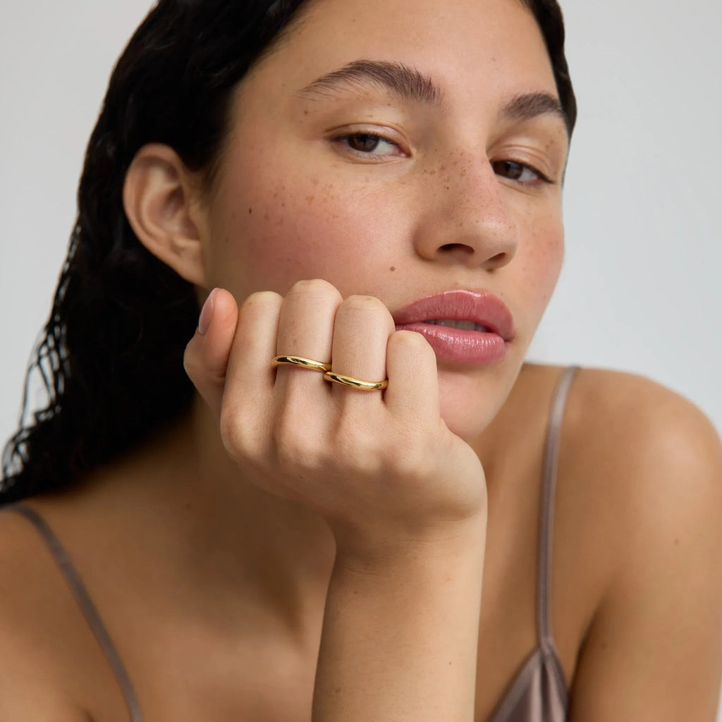 Close-up of woman with natural skin wearing two simple gold rings and a neutral strap top