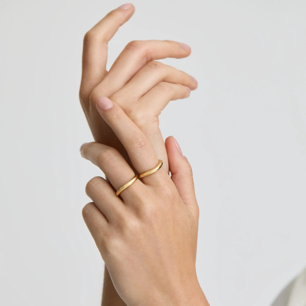Hands with two minimalist gold rings against a plain white background