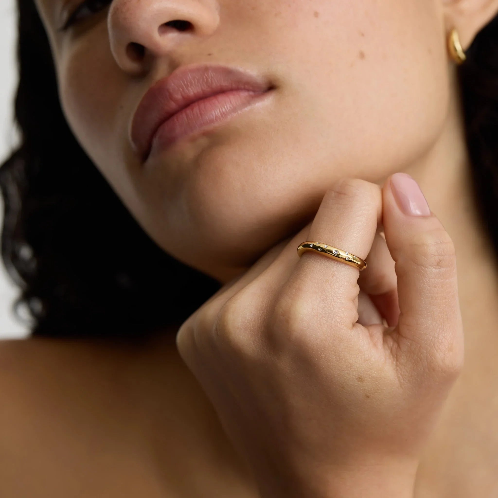 Close-up of woman wearing a gold ring with small diamonds on finger, showcasing minimalist jewelry