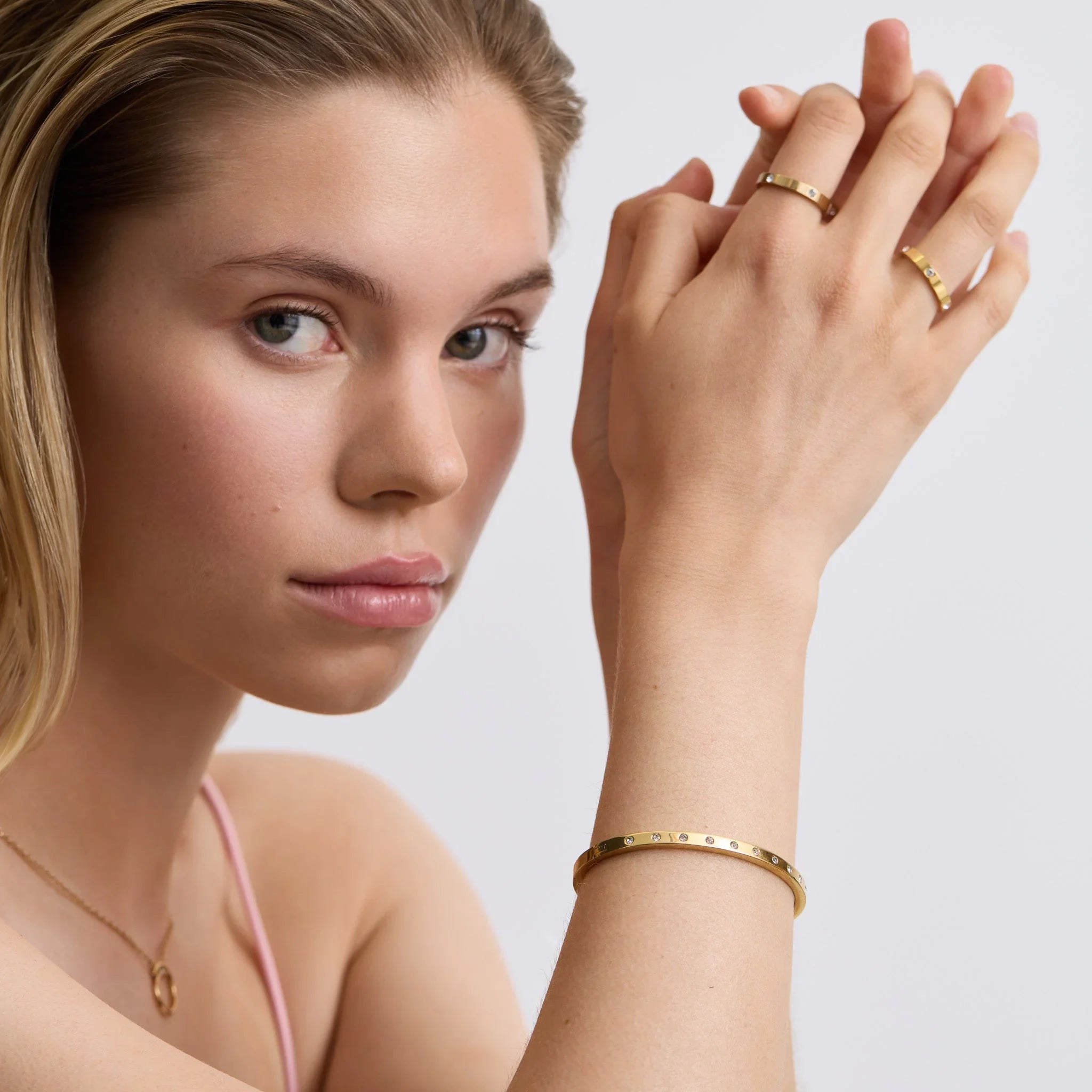 Woman wearing gold studded slim bangle bracelet and matching gold rings on hands, close-up portrait