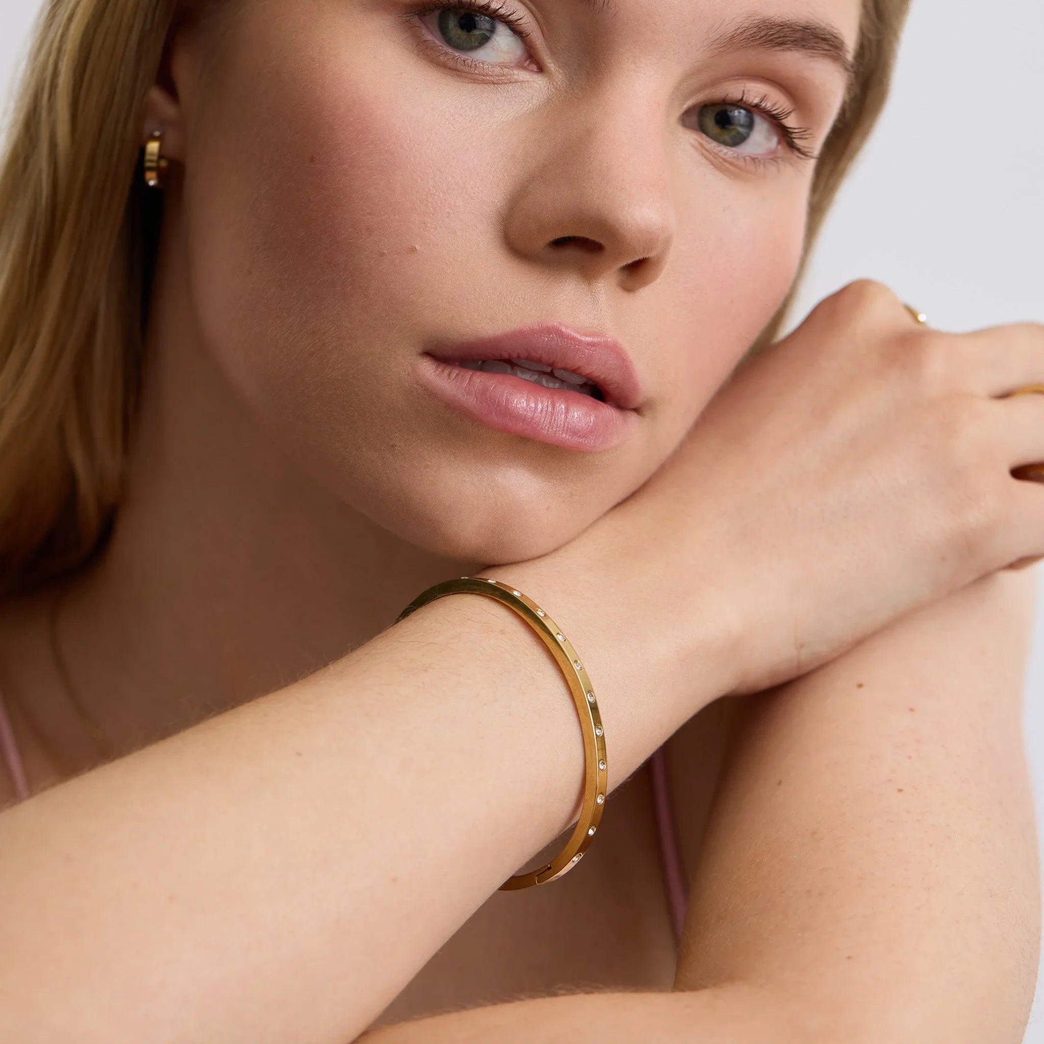 Close-up of a woman wearing a slim gold bangle with small embedded stones on her wrist