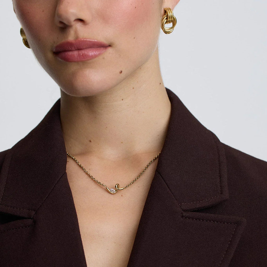 woman wearing gold twisted knot hoop earrings and delicate gold chain necklace with unique pendant