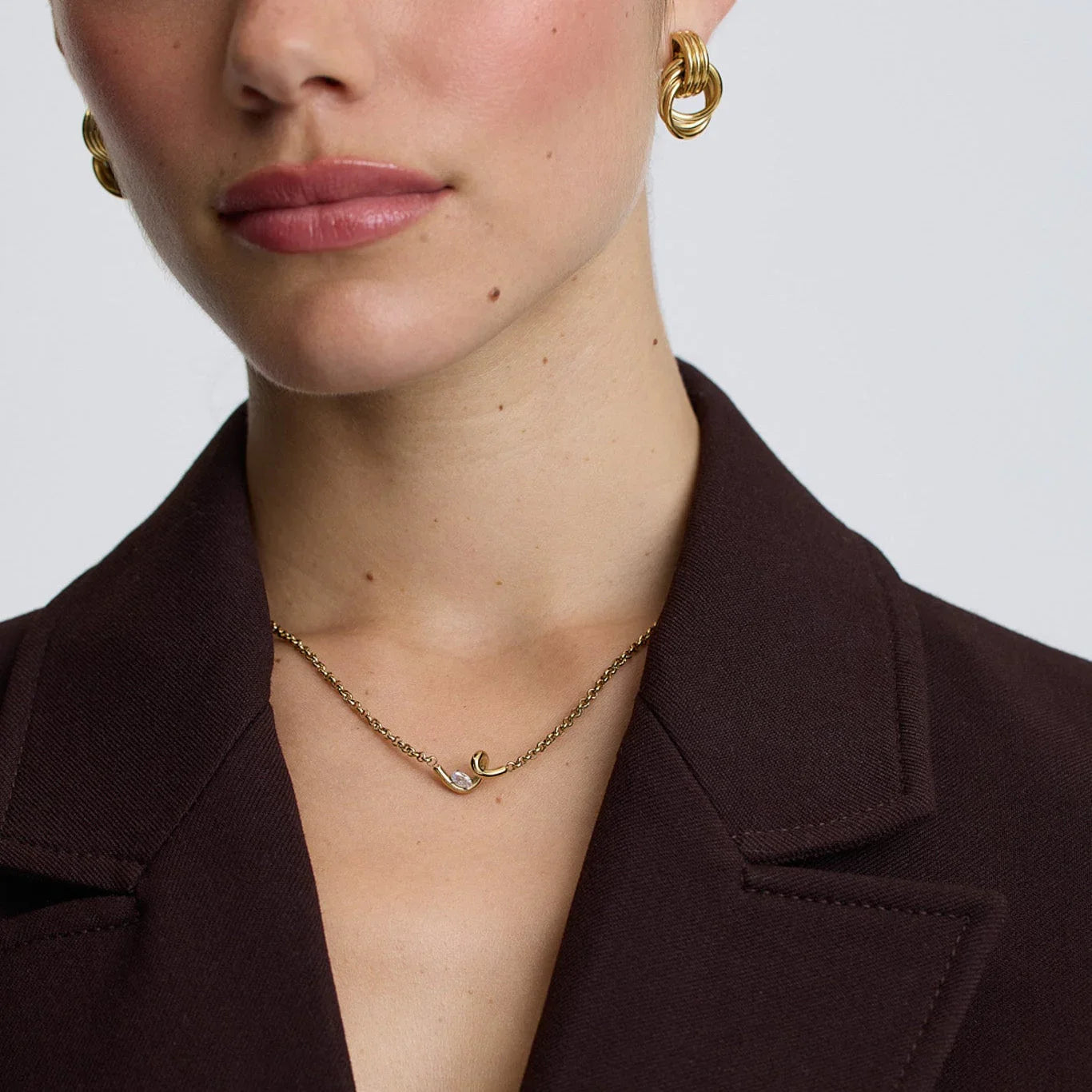 woman wearing gold twisted knot hoop earrings and delicate gold chain necklace with unique pendant