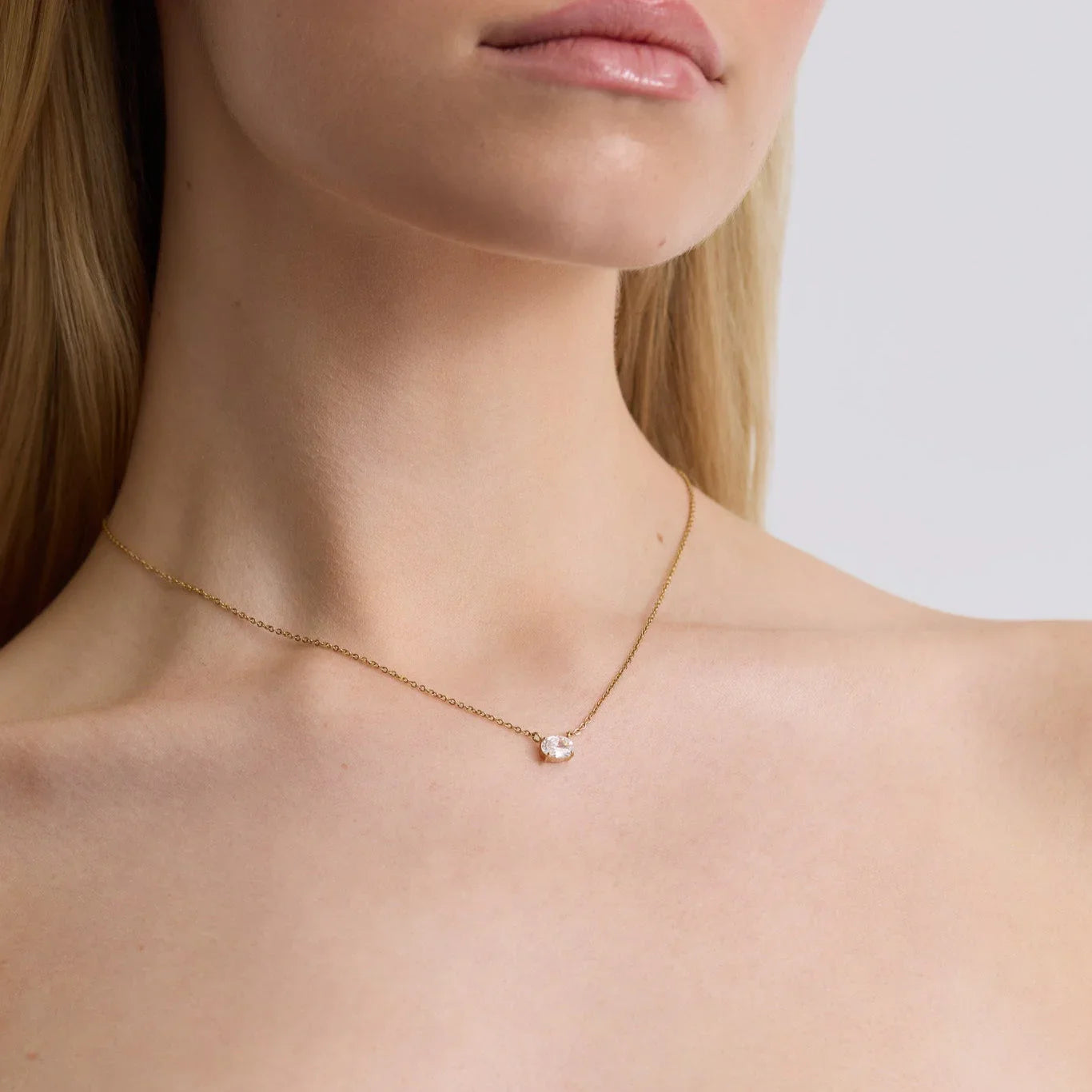 Close-up of a woman wearing a gold chain necklace with an oval solitaire diamond pendant
