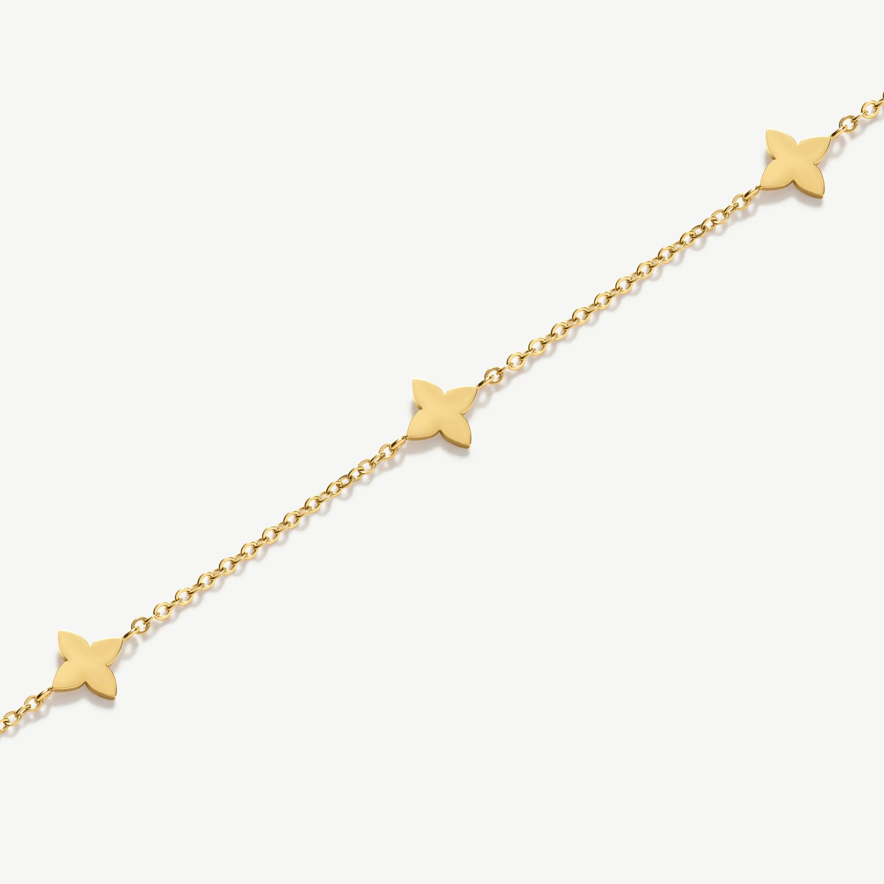 Delicate gold chain bracelet with three flat four-petal flower charms on white background