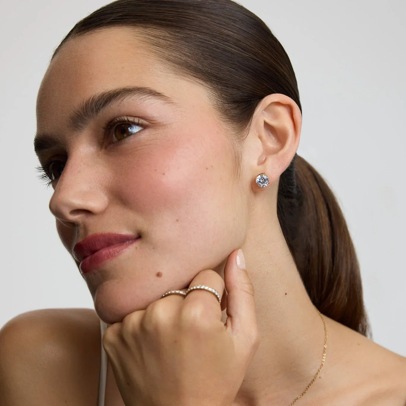 Close-up of woman wearing diamond stud earrings and pearl rings with hair tied back