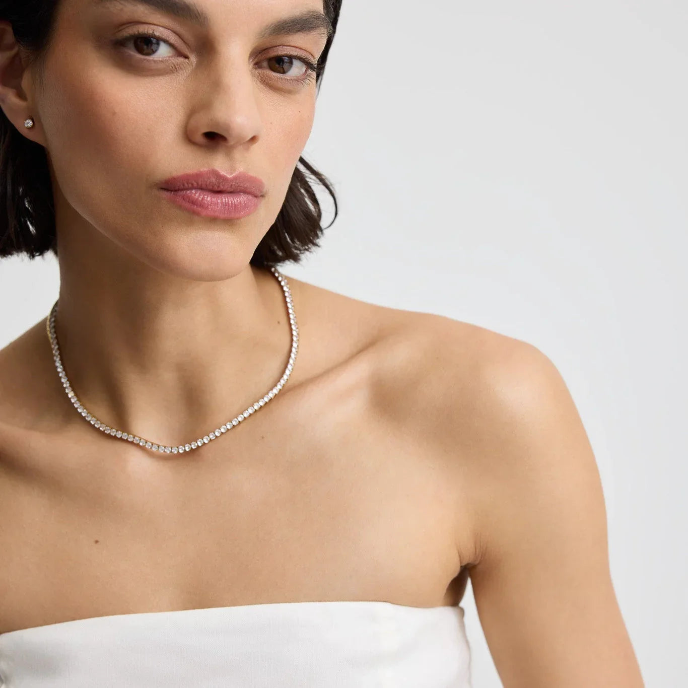 Close-up of woman wearing a diamond tennis necklace and stud earrings on bare shoulders