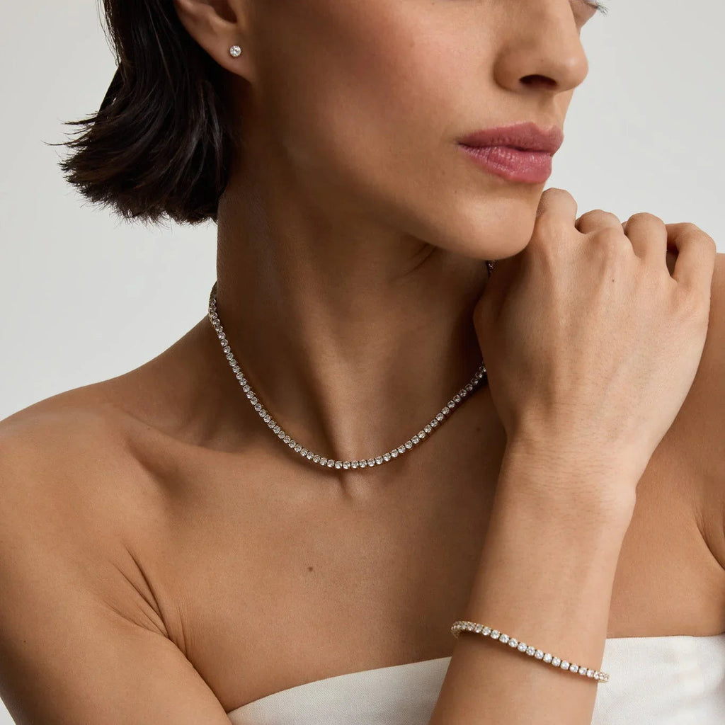 Close-up of woman wearing diamond tennis necklace, bracelet, and stud earrings on bare shoulders