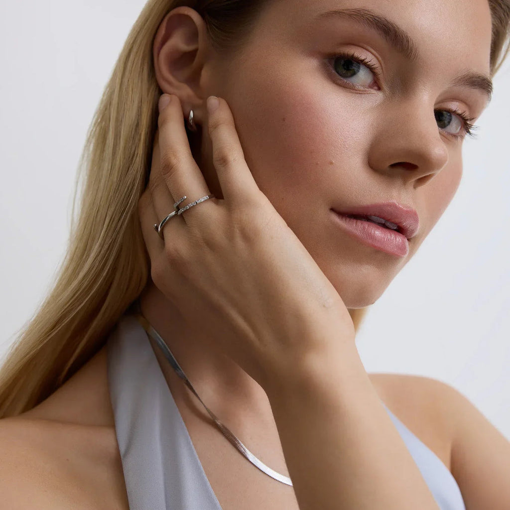 Close-up of woman wearing silver CZ wrap ring, silver hoop earring, silver necklace with pale blue top