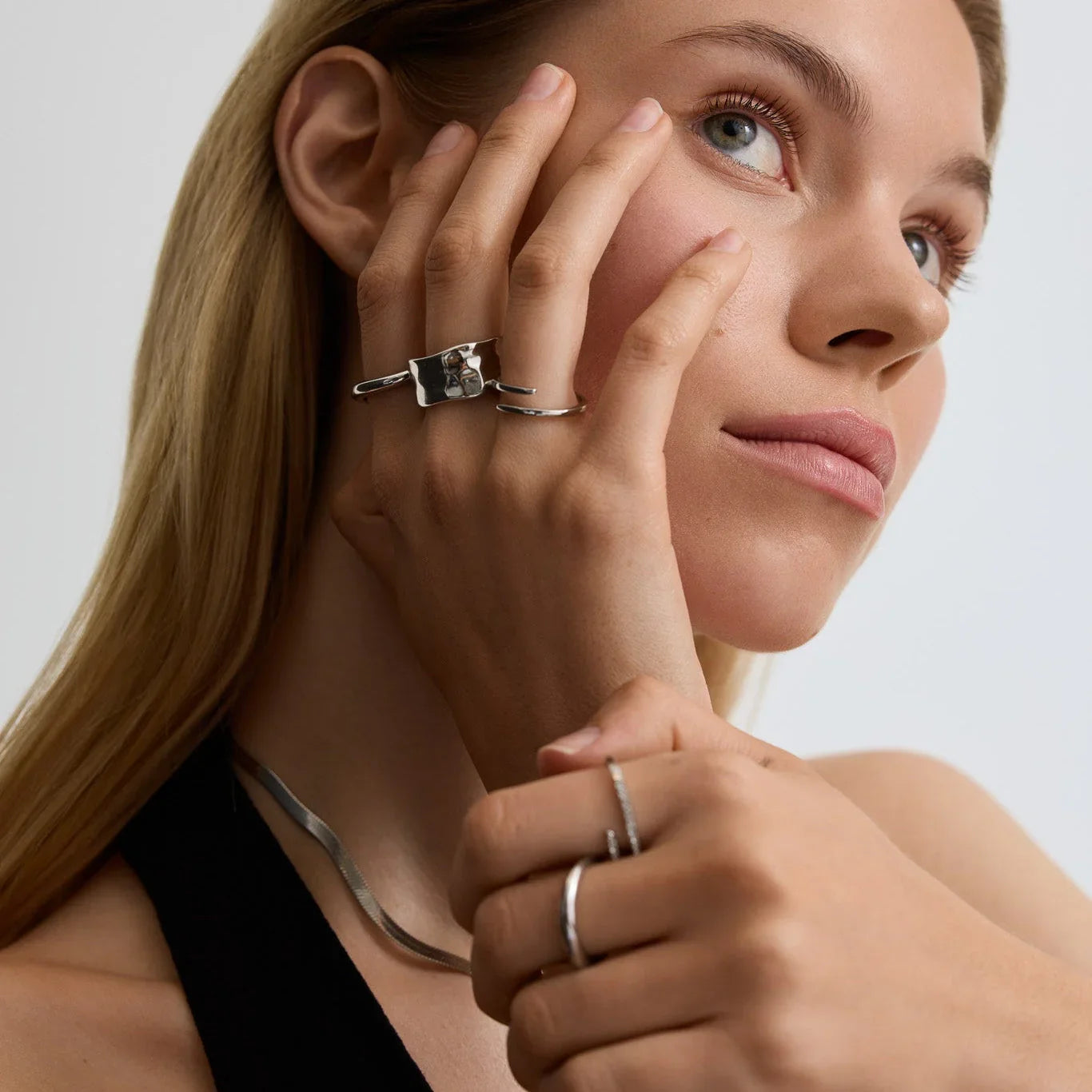 Close-up of woman wearing silver rings and a sleek silver necklace with natural makeup and long blonde hair